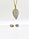 Close-up of a gold necklace with a crystal-studded leaf pendant and matching stud earrings.