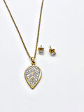 Close-up of a gold necklace with a crystal-studded leaf pendant and matching stud earrings.
